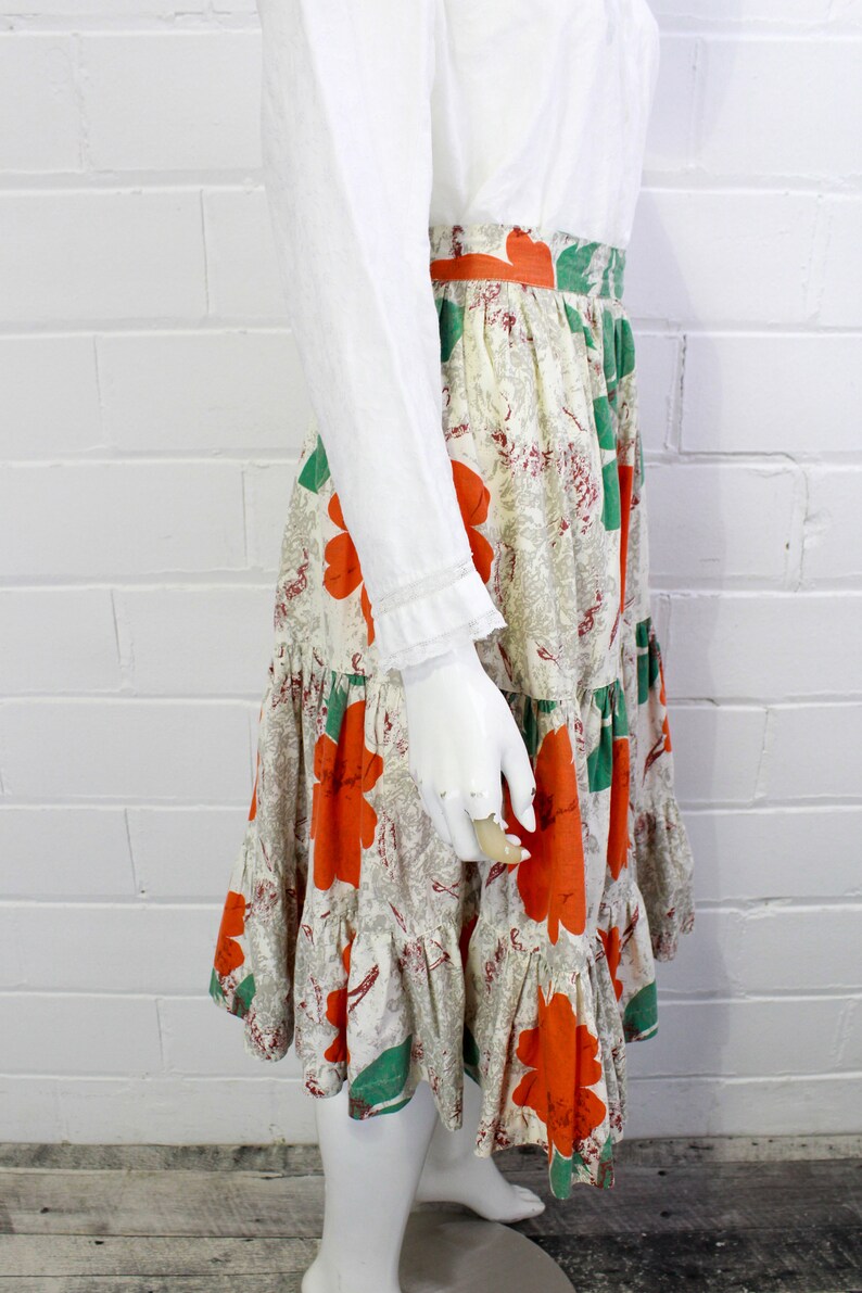 May include: A tiered skirt with a white background and a floral print featuring large orange flowers and green leaves.