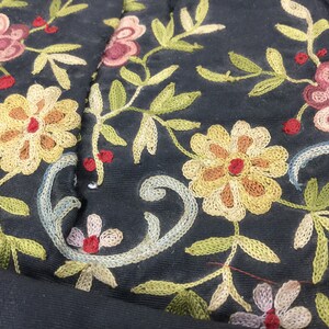Pode incluir: Close-up de tecido preto com bordado intrincado de flores e folhas em tons de amarelo, vermelho, verde e azul.