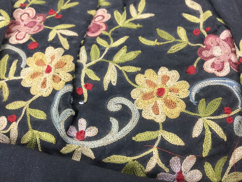 Pode incluir: Close-up de tecido preto com bordado intrincado de flores e folhas em tons de amarelo, vermelho, verde e azul.