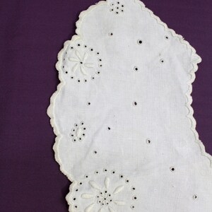 May include: White cotton lace doily with scalloped edges and embroidered floral designs. The doily is on a purple background.