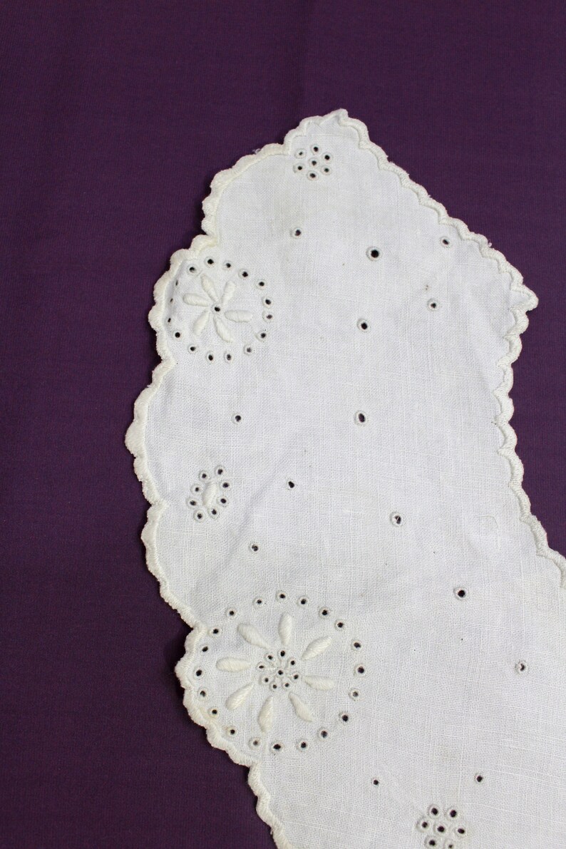 May include: White cotton lace doily with scalloped edges and embroidered floral designs. The doily is on a purple background.