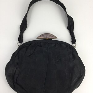 Pode incluir: Uma bolsa de noite de cetim preto com um fecho superior decorativo e adornado. A bolsa tem uma al&ccedil;a longa.