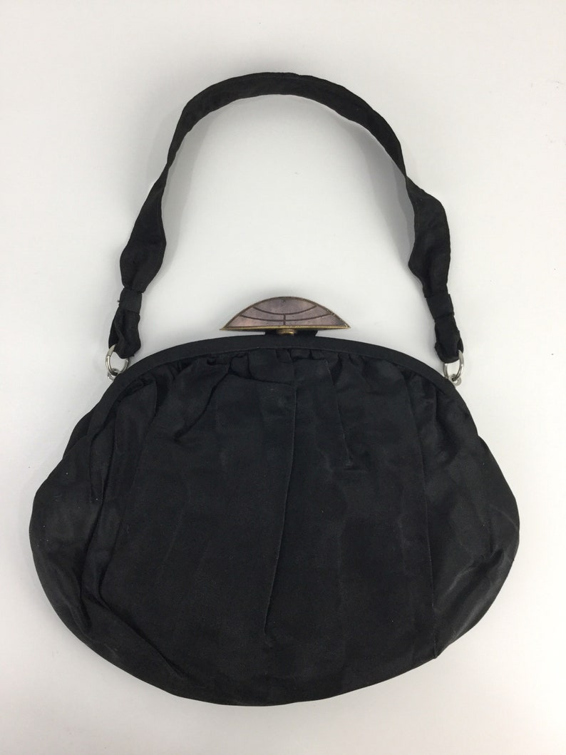 Pode incluir: Uma bolsa de noite de cetim preto com um fecho superior decorativo e adornado. A bolsa tem uma al&ccedil;a longa.