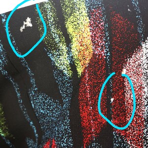 May include: Black fabric with a colorful abstract print. The print features streaks of red, yellow, green, and blue. There are small white specks throughout the fabric.