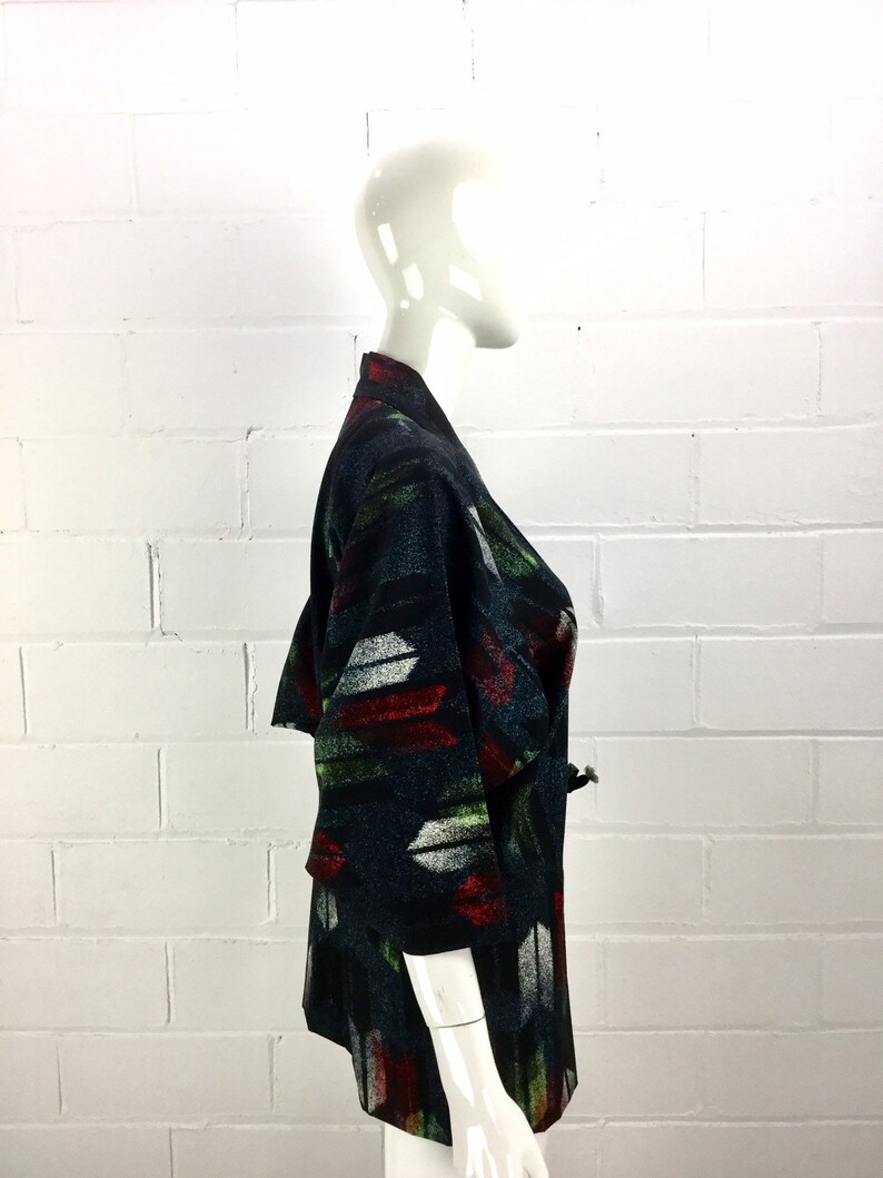 May include: A black and green patterned kimono with red, white, and green accents. The kimono is made of a soft, woven fabric and has a relaxed fit.