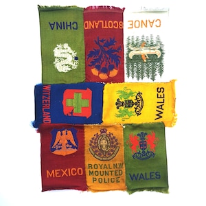 May include: A collection of nine colourful embroidered patches with various designs and text, including "Canoe Scotland China", "Switzerland", "Wales", "Mexico", "Royal NW Mounted Police", and "Wales".