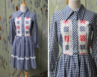May include: A blue and white gingham dress with red and white gingham accents and white lace trim. The dress has a collared neckline and long sleeves.