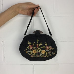 Pode incluir: Uma bolsa preta bordada com um design floral. A bolsa tem uma al&ccedil;a superior e um fecho de encaixe.