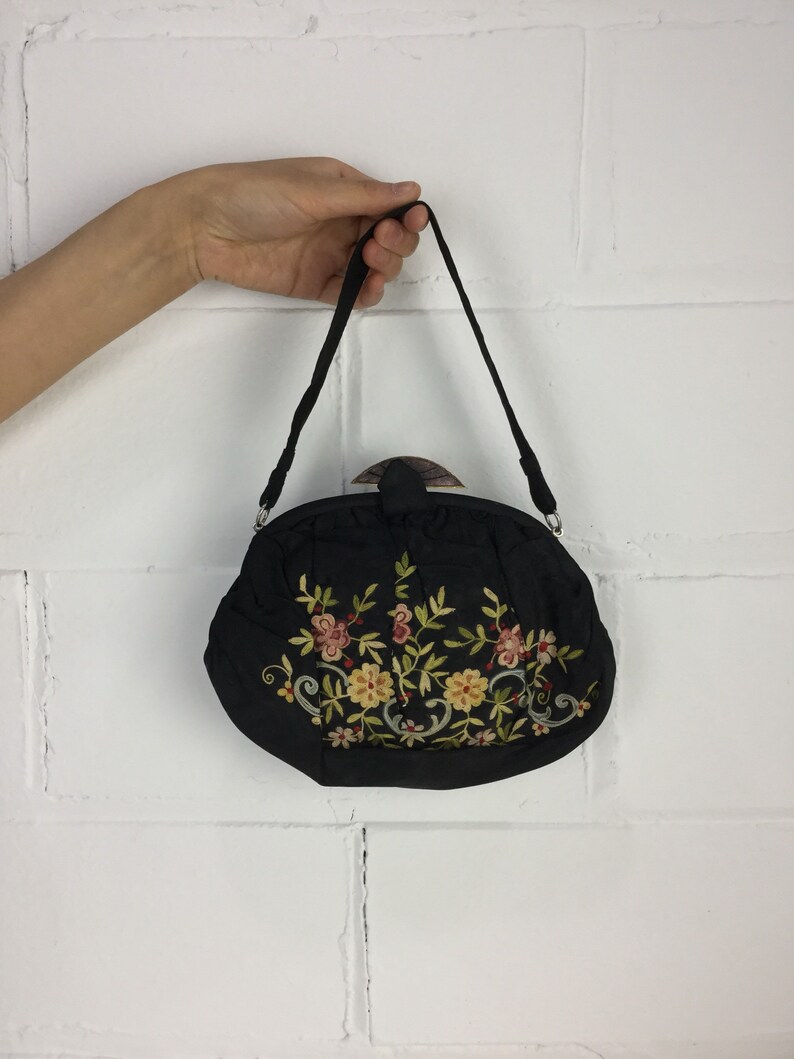 Pode incluir: Uma bolsa preta bordada com um design floral. A bolsa tem uma al&ccedil;a superior e um fecho de encaixe.