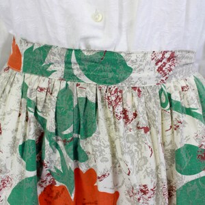 May include: A white skirt with a green and orange floral print. The skirt has a gathered waist and a full skirt.