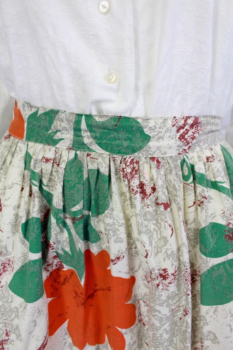 May include: A white skirt with a green and orange floral print. The skirt has a gathered waist and a full skirt.
