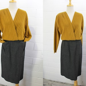 May include: A mustard yellow sweater with a wrap style neckline and long sleeves, paired with a charcoal grey skirt with pockets.