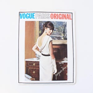 May include: A vintage Vogue Paris Original sewing pattern for a white dress with a low back, designed by Jacques Heim. The pattern number is 1574.
