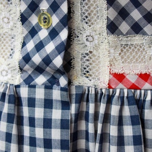 Puede incluir: Un vestido de cuadros azules y blancos con ribete de encaje blanco y ribete de cuadros rojos y blancos. El vestido tiene un cierre de bot&oacute;n en la parte superior.
