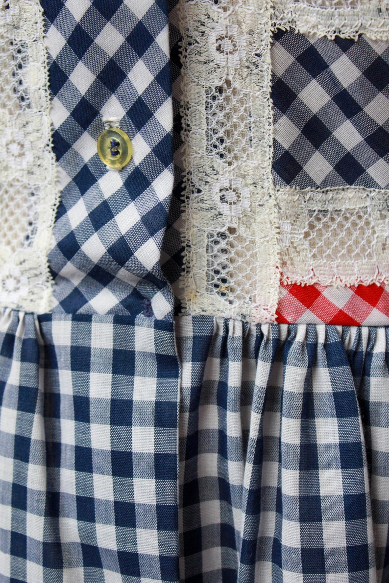 Puede incluir: Un vestido de cuadros azules y blancos con ribete de encaje blanco y ribete de cuadros rojos y blancos. El vestido tiene un cierre de bot&oacute;n en la parte superior.