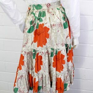 May include: A tiered skirt with a white background and a floral print featuring large orange flowers and green leaves.