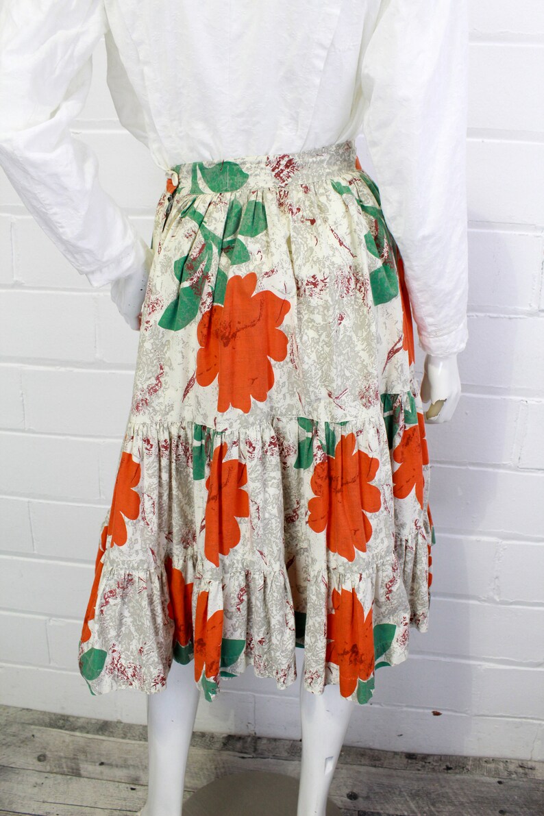 May include: A tiered skirt with a white background and a floral print featuring large orange flowers and green leaves.