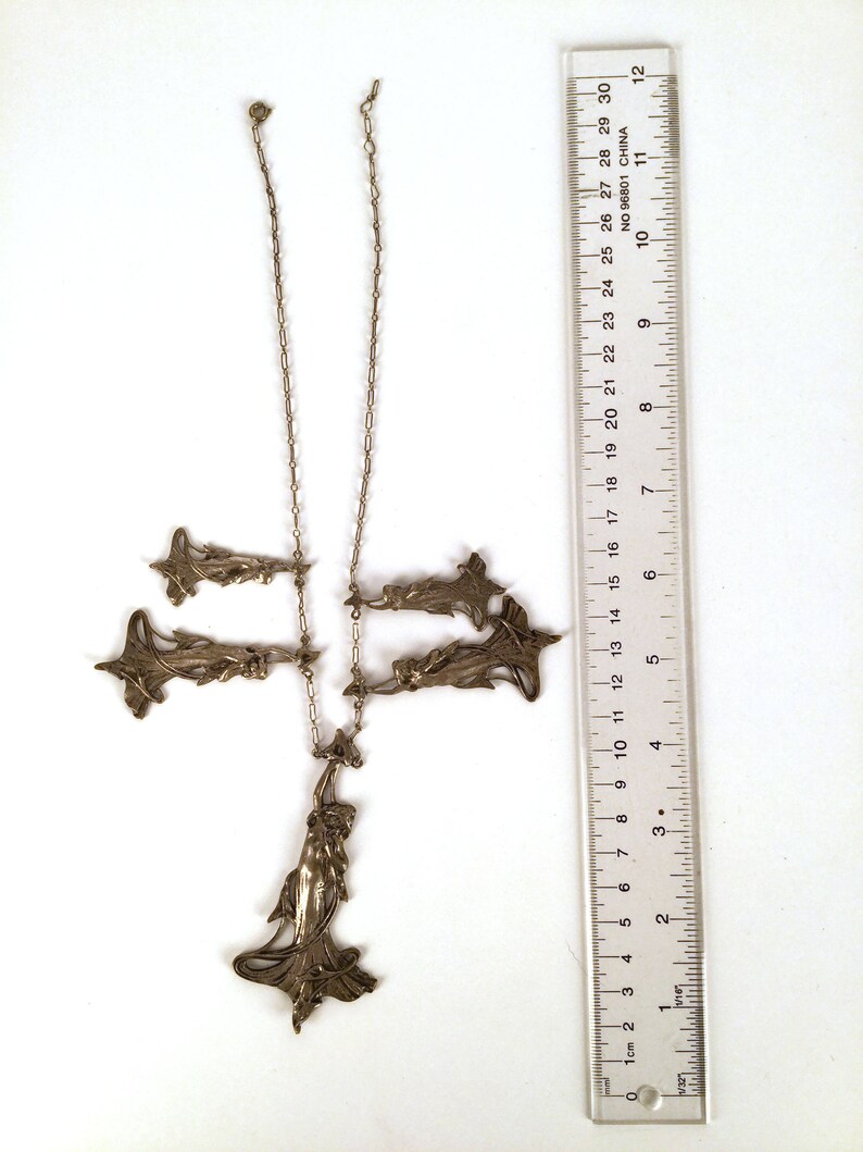 May include: A silver necklace with a pendant featuring a stylised female figure and several smaller pendants in the shape of stylised flowers. The necklace is approximately 28 inches long.