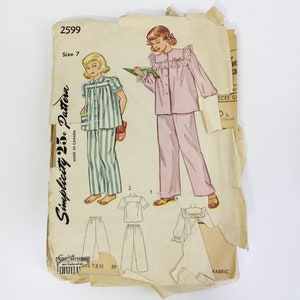 May include: Vintage Simplicity sewing pattern number 2599, size 7, for a girl's pyjamas. The pattern shows two girls wearing pyjamas, one in pink and one in blue and white stripes. The pattern includes instructions for making a top and trousers.