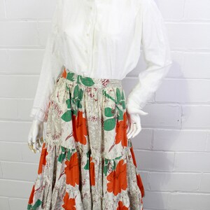 May include: A white button-up shirt with a peter pan collar paired with a tiered skirt featuring a floral print in shades of orange, green, and beige.