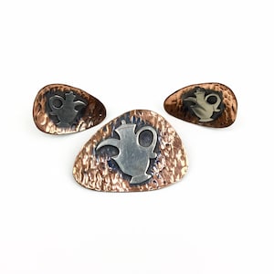 May include: Three hammered copper and silver brooches featuring a teapot design. The brooches are in shades of copper and silver.