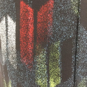 May include: Abstract fabric with a black background and colorful vertical stripes. The stripes are red, white, green, and blue. The fabric has a speckled texture.