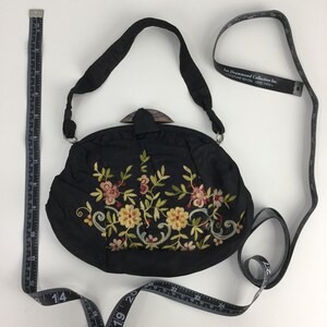 Pode incluir: Bolsa de noite de cetim preto bordada com um design floral e um fecho de madeira. A bolsa tem uma al&ccedil;a comprida e mede 18 cm de di&acirc;metro.