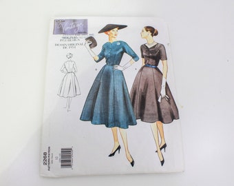 May include: Vintage sewing pattern for a dress with a full skirt. The pattern is for sizes 12-18 and is from 1951. The pattern shows two women wearing the dress, one in a blue and white gingham print and the other in a solid black.