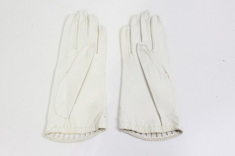 May include: A pair of white leather gloves with a ribbed cuff.