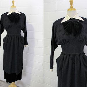 Pode incluir: Um vestido preto com colarinho branco e um laço de veludo preto. O vestido tem um corpete justo e uma saia cheia. O vestido é feito de um tecido texturizado.