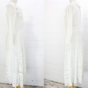 May include: A white maxi dress with long sleeves and a lace trim. The dress has a ruffled collar and a fitted bodice.