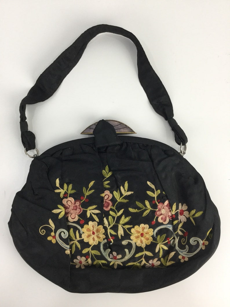Pode incluir: Uma bolsa de m&atilde;o de tecido preto com um design bordado floral. A bolsa tem um fecho superior e uma al&ccedil;a longa.