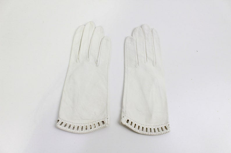 May include: A pair of white leather gloves with a decorative lace trim around the wrist.