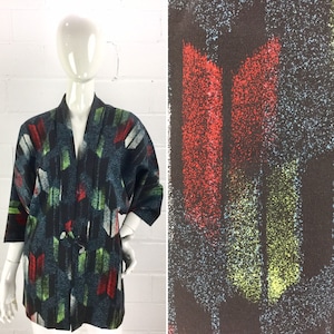 May include: A black and blue kimono with a colorful abstract print featuring red, green, and white geometric shapes. The kimono has a wide, open collar and three-quarter sleeves.