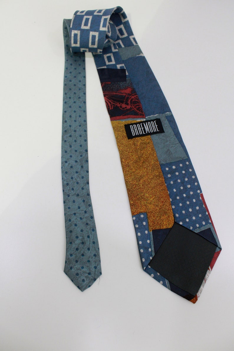 May include: A patterned necktie with a variety of blue hues and a polka dot design. The tie features a patchwork design with squares, rectangles, and a bicycle graphic. The label reads "BRAEMORE".