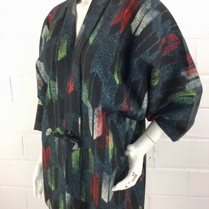 May include: A black kimono with a colorful abstract print. The print features brushstrokes of red, green, and white on a dark blue background.