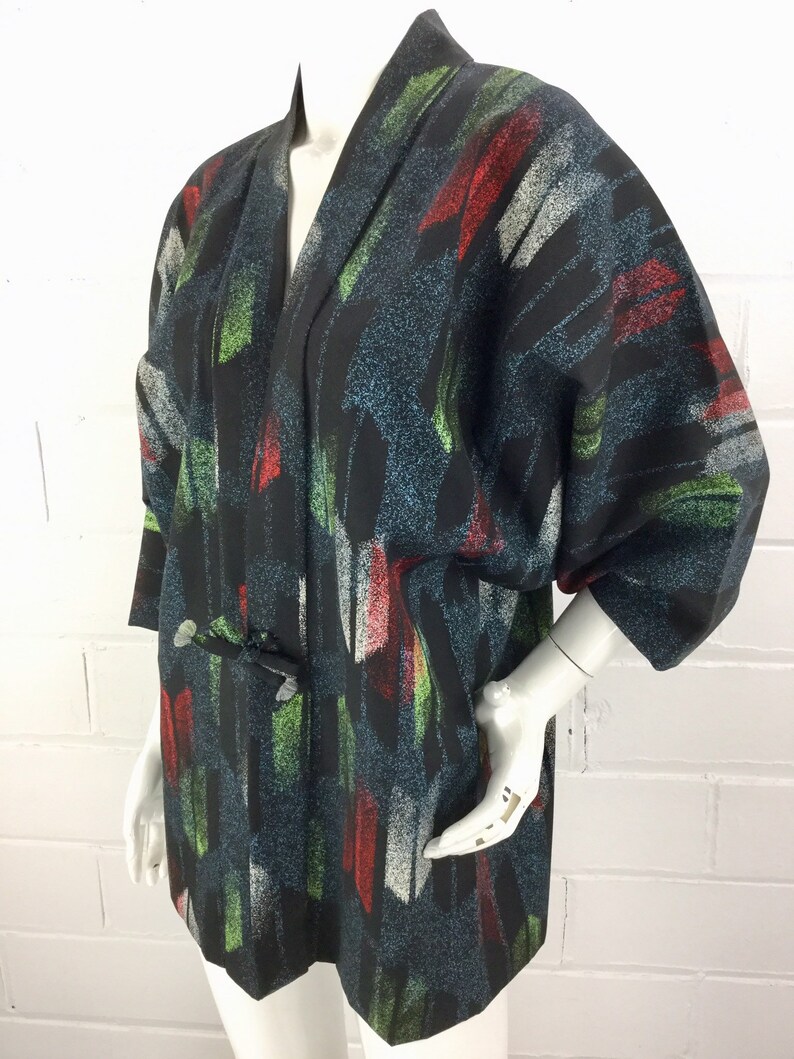 May include: A black kimono with a colorful abstract print. The print features brushstrokes of red, green, and white on a dark blue background.