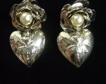 May include: A pair of silver earrings featuring a rose design and a ballerina figure in the centre of a heart-shaped pendant.