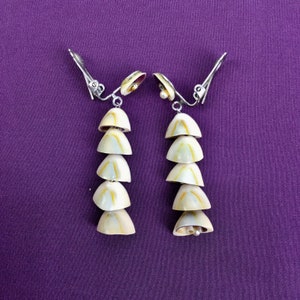 May include: A pair of silver clip-on earrings with a cascade of six white seashells, each with a subtle yellow and brown pattern.