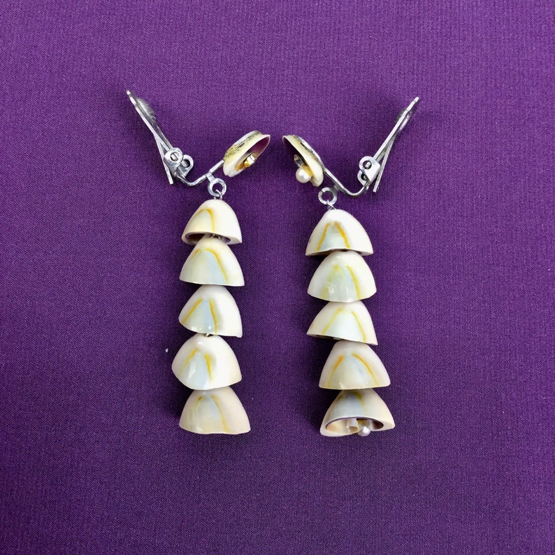 May include: A pair of silver clip-on earrings with a cascade of six white seashells, each with a subtle yellow and brown pattern.