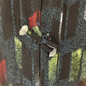 May include: Black fabric with a colorful abstract print. The fabric has a textured surface and a tie closure.