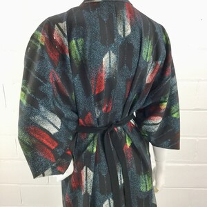 May include: A black kimono with a colorful abstract print featuring red, green, and white brushstrokes. The kimono has a black sash.