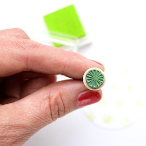Peut inclure: Gros plan sur un tampon en caoutchouc rond vert et blanc avec un motif circulaire. Le tampon est tenu par une main.