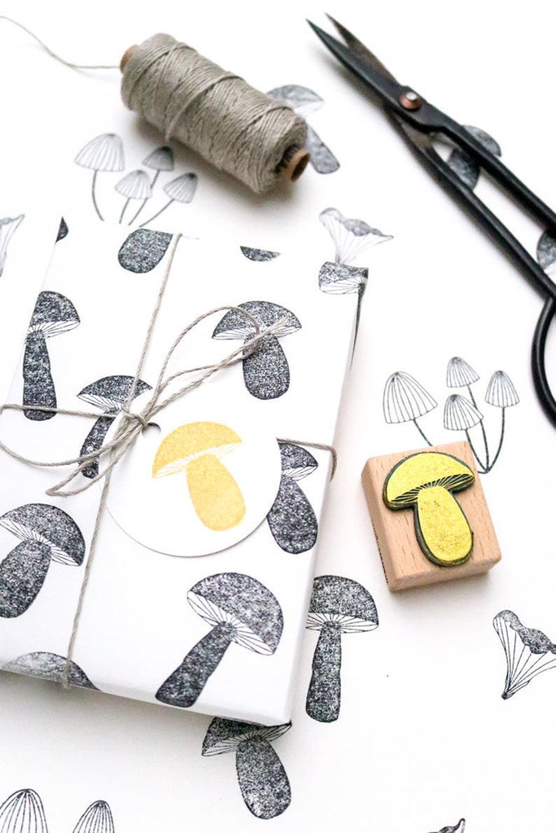 May include: A white gift box with a black and white mushroom pattern. The box is tied with twine and has a round, yellow mushroom sticker. A wooden stamp with a yellow mushroom design is also shown.