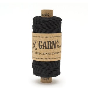 Könnte beinhalten: Eine Spule schwarzes Garn mit einem braunen Etikett, auf dem "GARN & mehr" und "TWINE - LEINEN - ZWIRN - FADEN" steht.
