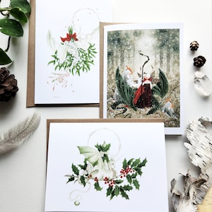 May include: Three holiday cards featuring white dragons with red bows and holly leaves. The cards are blank inside and ready for writing.