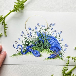 K&ouml;nnte beinhalten: Ein Aquarellbild eines blauen Drachen, der sich in einem Bett aus Vergissmeinnicht-Blumen zusammenrollt. Der Drache tr&auml;gt eine goldene Krone und ist von gr&uuml;nen Bl&auml;ttern umgeben. Das Bild ist signiert mit "Grimshaw" und "Forget-Me-Not Dragon".