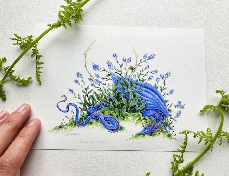 K&ouml;nnte beinhalten: Ein Aquarellbild eines blauen Drachen, der sich in einem Bett aus Vergissmeinnicht-Blumen zusammenrollt. Der Drache tr&auml;gt eine goldene Krone und ist von gr&uuml;nen Bl&auml;ttern umgeben. Das Bild ist signiert mit "Grimshaw" und "Forget-Me-Not Dragon".