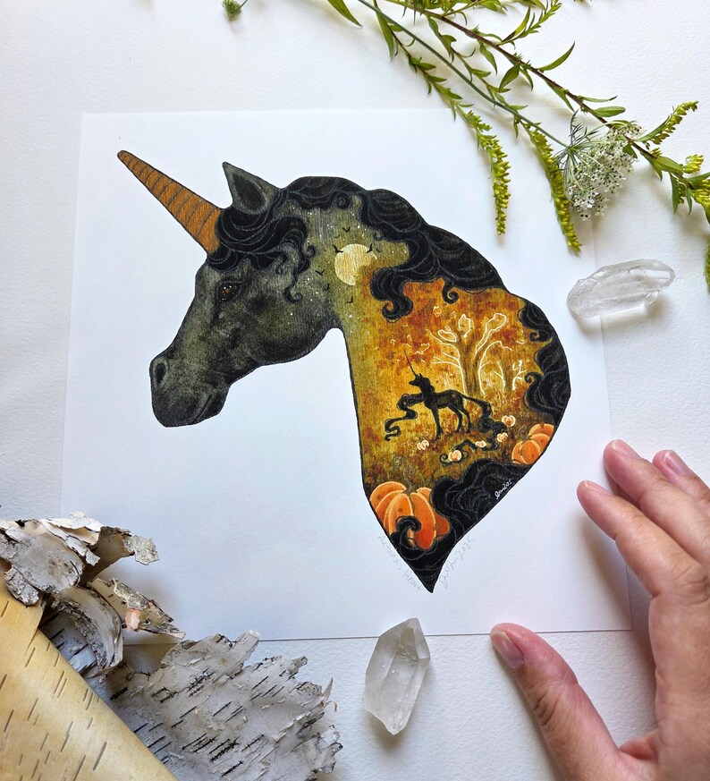 May include: A watercolor illustration of a unicorn head with a golden horn and black mane. The interior of the unicorn's head features a fall scene with a black unicorn, pumpkins, and a tree. The artwork is set against a white background.