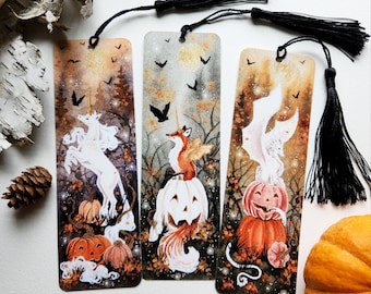 Puede incluir: Tres marcadores de libros con temática de Halloween con ilustraciones de acuarela. El primer marcador presenta un unicornio blanco con un cuerno dorado, el segundo marcador presenta un zorro con alas sentado en una calabaza tallada, y el tercer marcador presenta un unicornio blanco con alas sentado en una calabaza tallada.